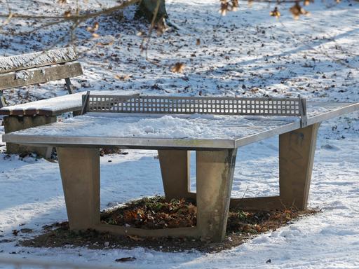 Eine verschneite Tischtennisplatte im Winter in einem Park. 