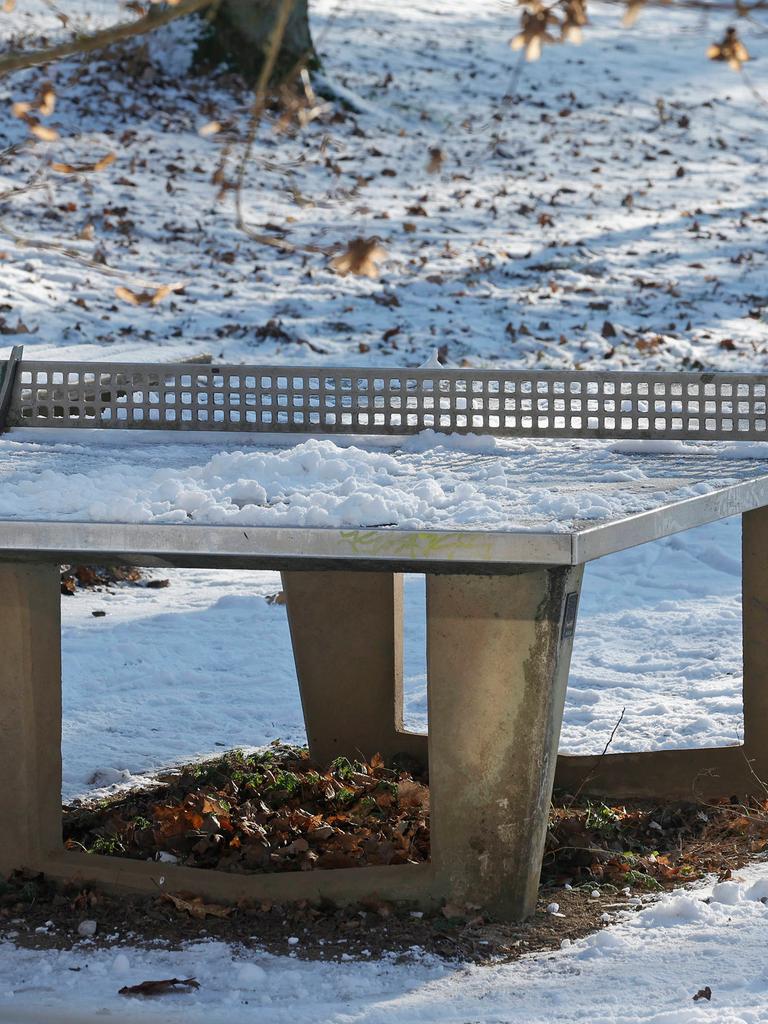 Eine verschneite Tischtennisplatte im Winter in einem Park. 