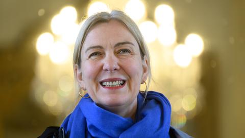 Eine lächelnde blonde Frau mit Ohringen und Schal.