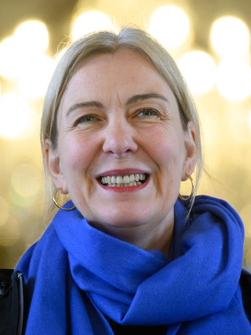 Eine lächelnde blonde Frau mit Ohringen und Schal.