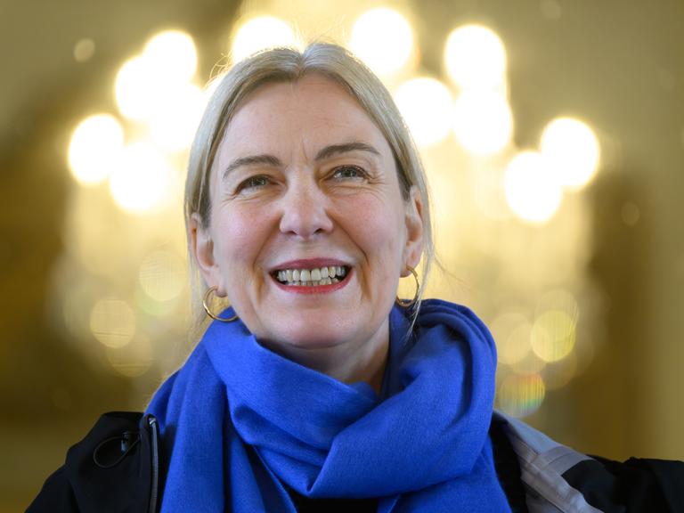 Eine lächelnde blonde Frau mit Ohringen und Schal.