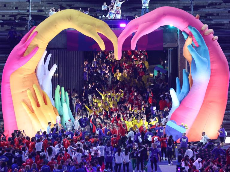 Die Eröffnungs-Feier von den Special Olympics in Berlin. Die Sportlerinnen und Sportler laufen durch zwei aufblasbare bunte Hände. Sie formen ein Herz.