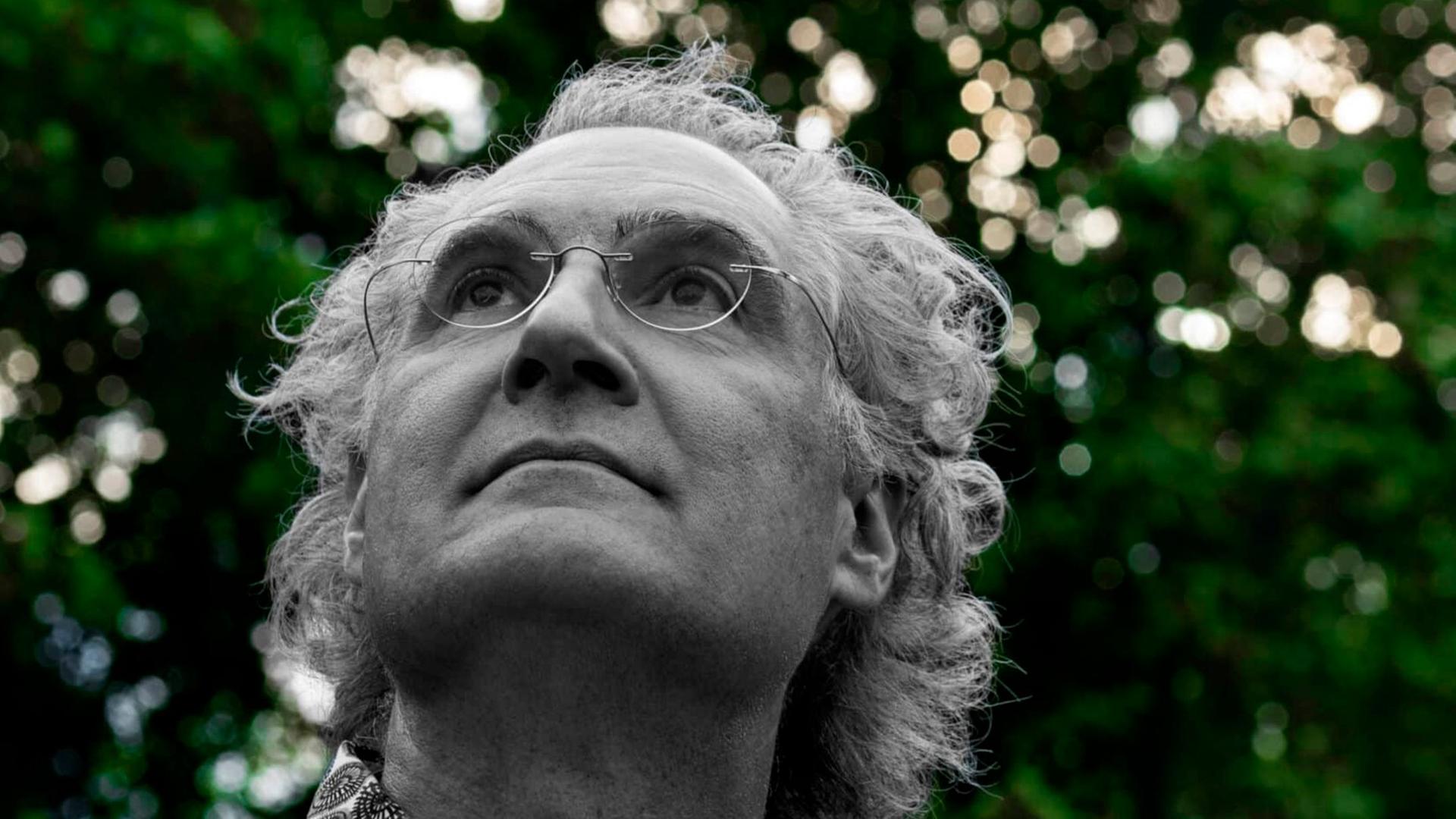 Matthias Kirschnereit blickt in den Himmel vor einer Baumgruppe, während diese grün erscheint, ist er in schwarz-weiß zu sehen.
