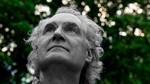 Matthias Kirschnereit blickt in den Himmel vor einer Baumgruppe, während diese grün erscheint, ist er in schwarz-weiß zu sehen.