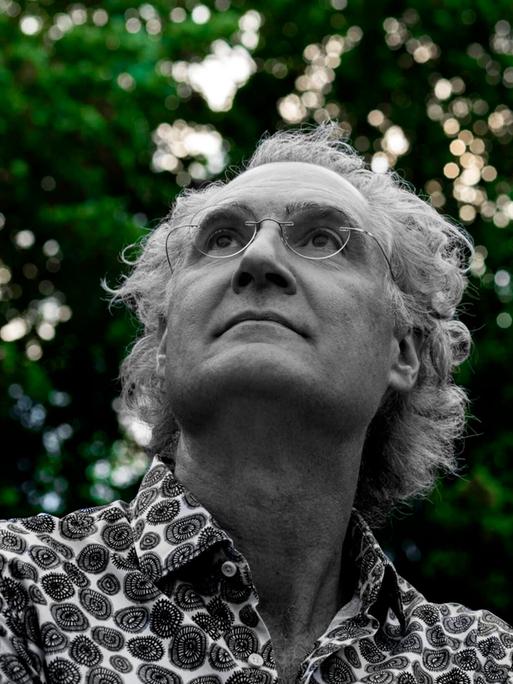 Matthias Kirschnereit blickt in den Himmel vor einer Baumgruppe, während diese grün erscheint, ist er in schwarz-weiß zu sehen.