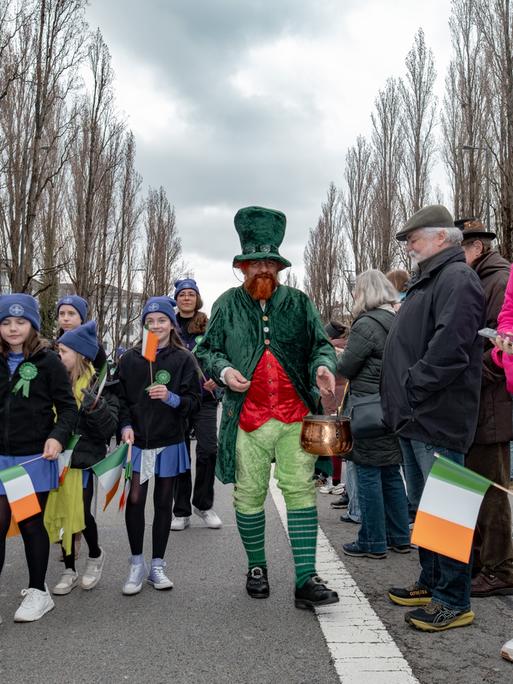 Teilnehmer der St. Patrick's Day Parade in München laufen verkleidet und mit irischen Flaggen über eine Straße.