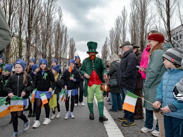 Teilnehmer der St. Patrick's Day Parade in München laufen verkleidet und mit irischen Flaggen über eine Straße.