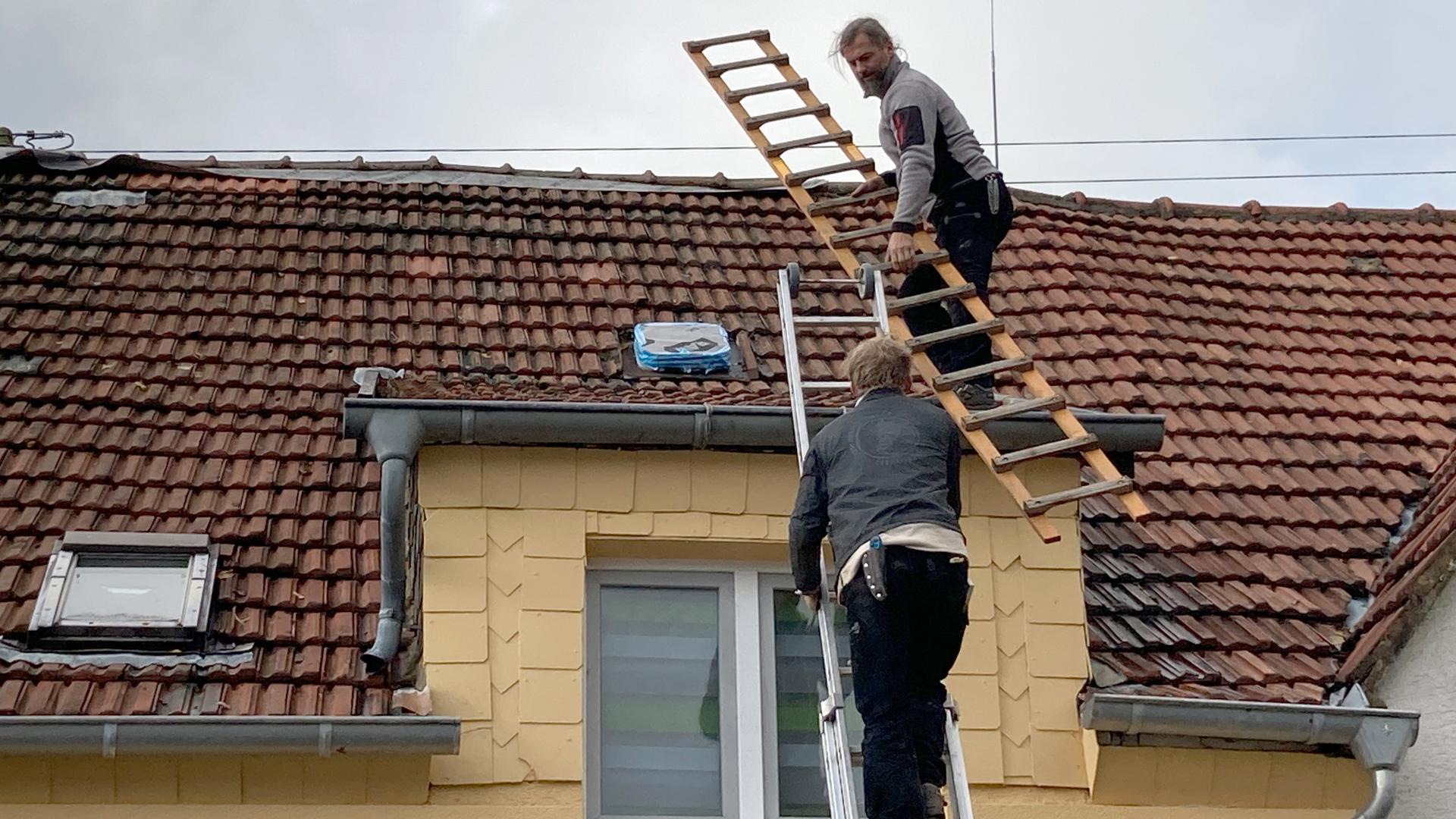 Zwei Dackdecker steigen auf ein Hausdach hinauf, um es zu reparieren. 