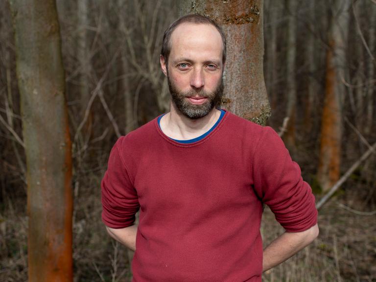 Thomas Weiler steht an einem Baum gelehnt im Wald