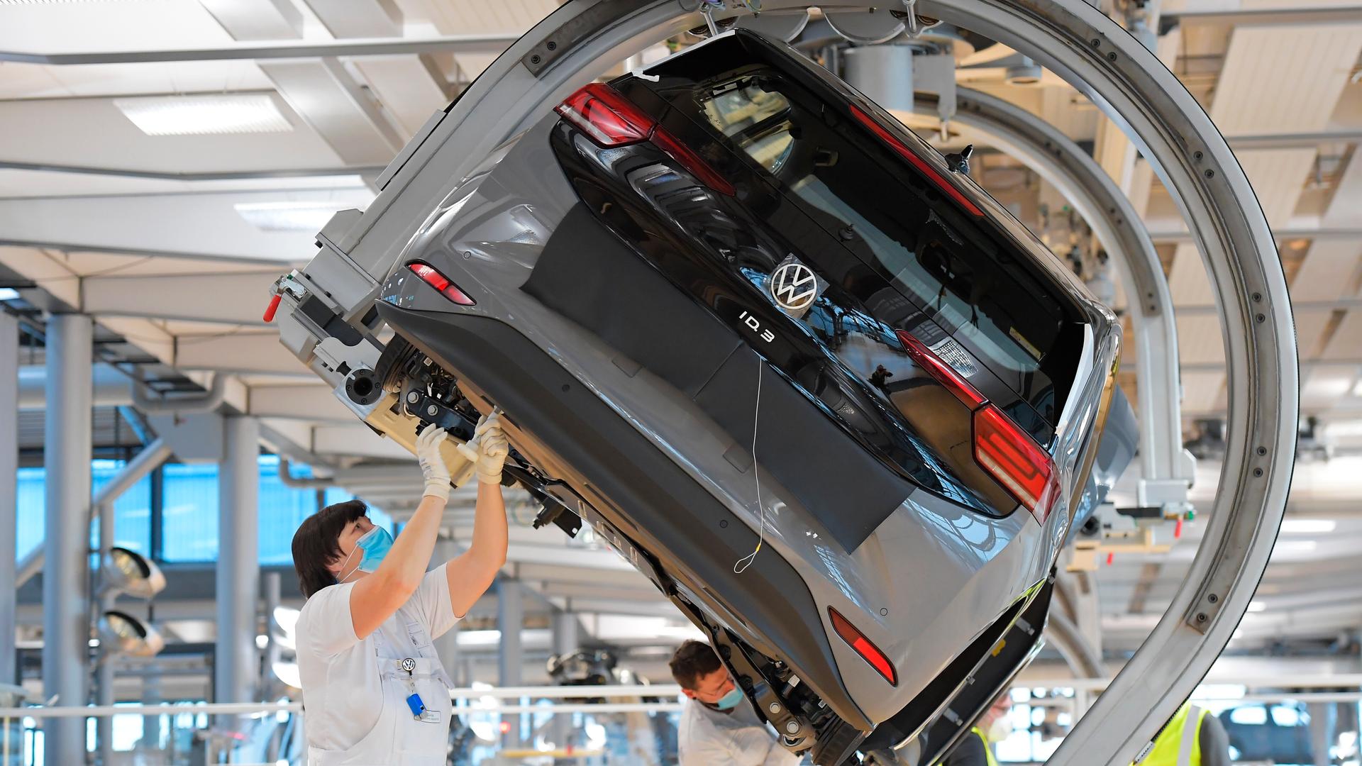 VW-Angestellte stehen in einer Fabrik unter einem Auto arbeiten an dem Wagen.