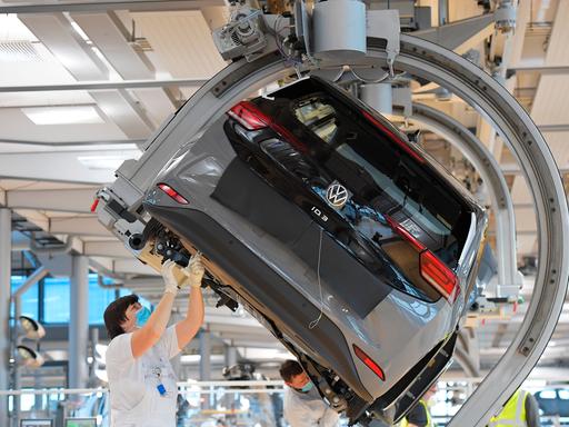 VW-Angestellte stehen in einer Fabrik unter einem Auto arbeiten an dem Wagen.