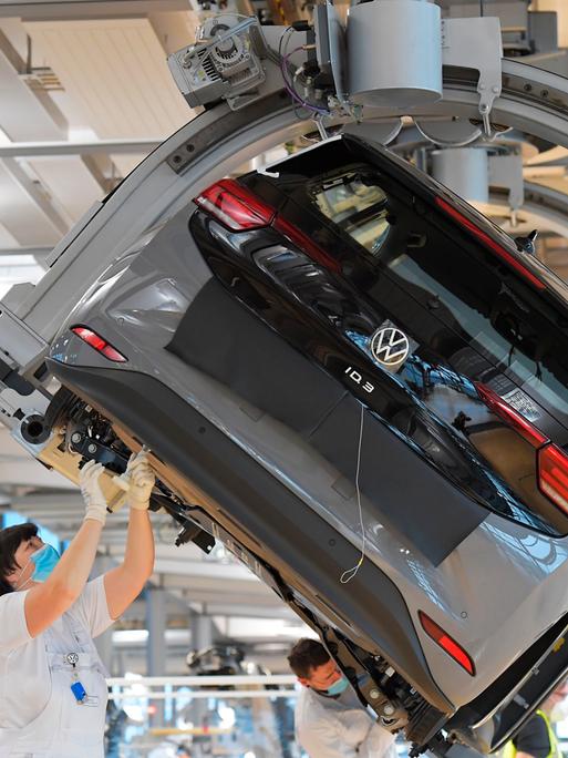 VW-Angestellte stehen in einer Fabrik unter einem Auto arbeiten an dem Wagen.