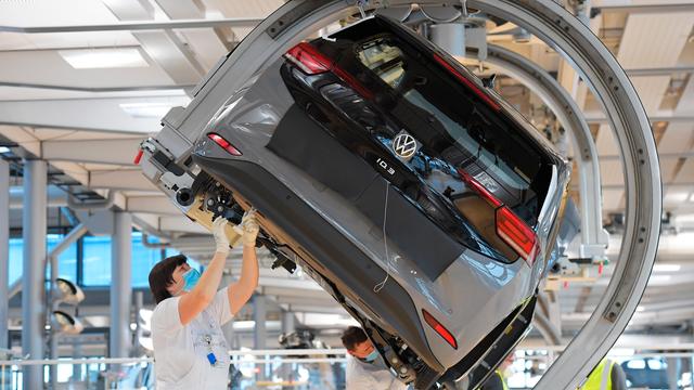 VW-Angestellte stehen in einer Fabrik unter einem Auto arbeiten an dem Wagen.