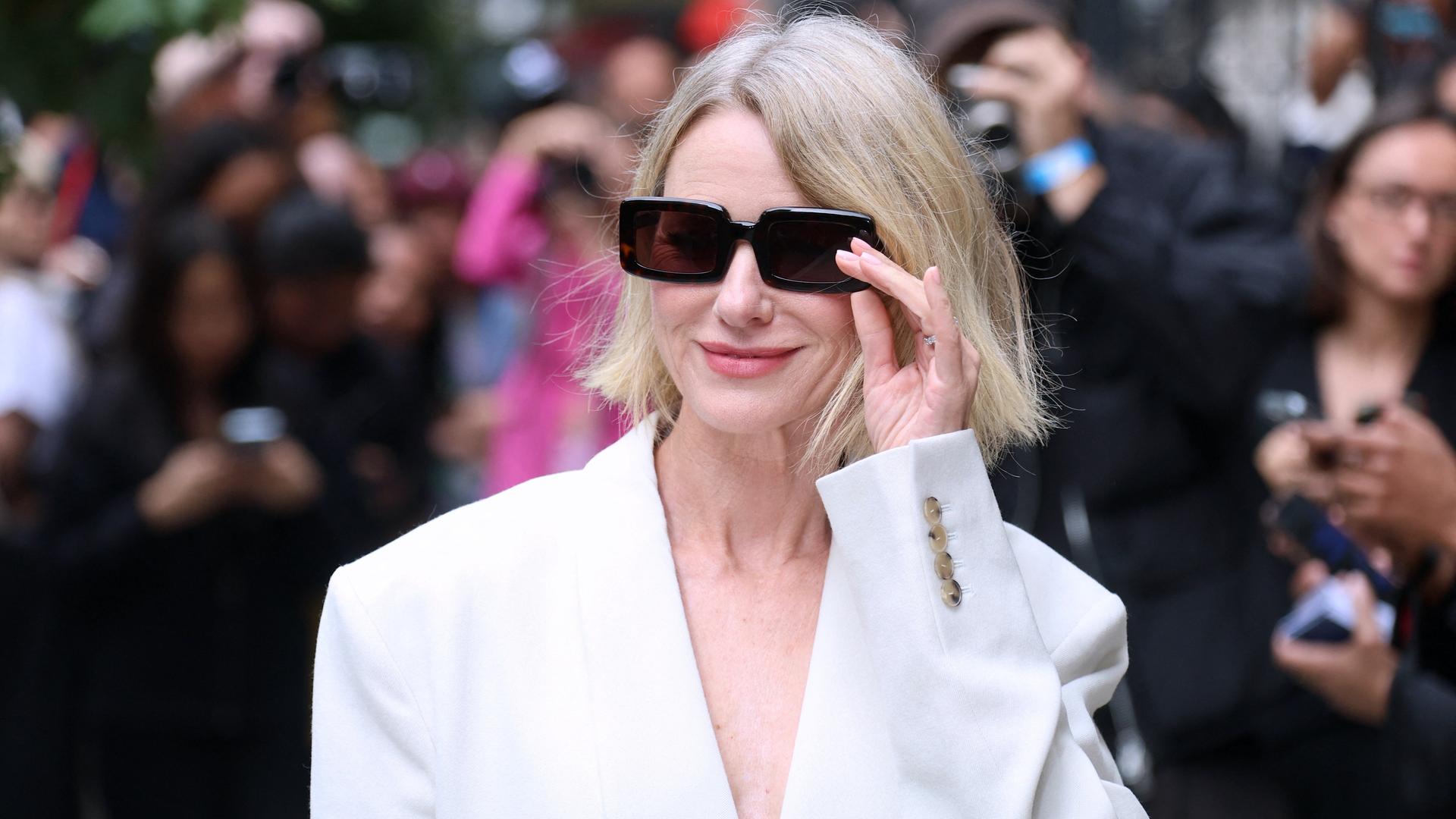 Die Schauspielerin Naomi Watts trägt eine schwarze Sonnenbrille und einen weißen Blazer bei der Fashion Week in New York. Sie lächelt in die Kamera. Die Schauspielerin Naomi Watts trägt eine schwarze Sonnenbrille und einen weißen Blazer bei der Fashion Week in New York. Sie lächelt in die Kamera.
