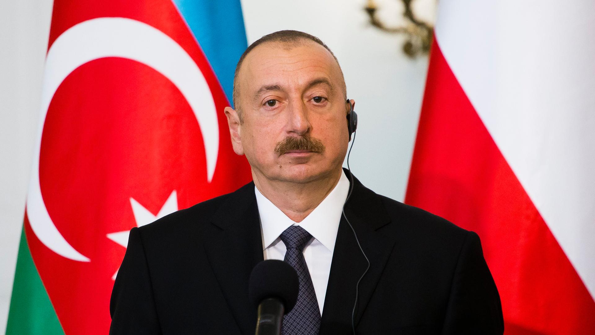 Der aserbaidschanische Präsident Ilham Alijew steht vor Flaggen.