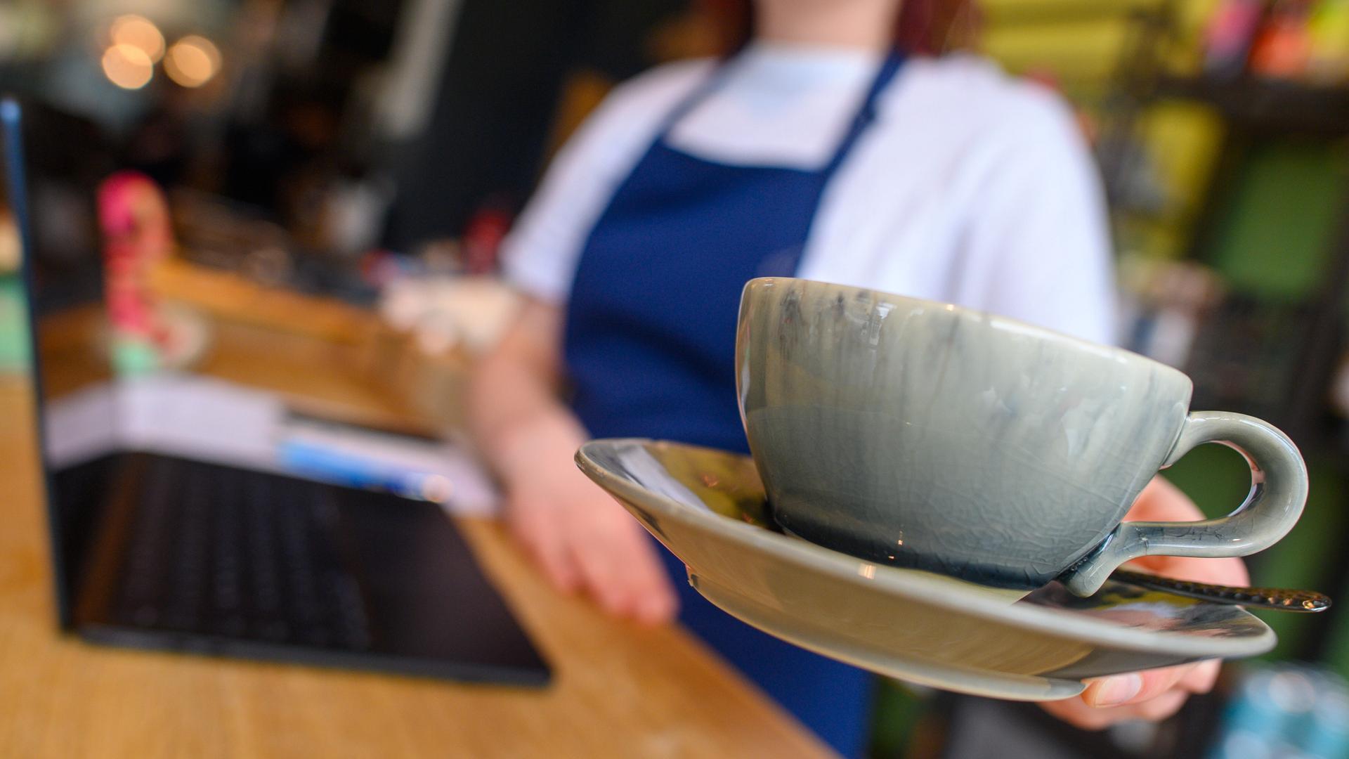 Eine Bedienung bringt in einem Café eine Tasse an einen Tisch. Eine Bedienung bringt in einem Café eine Tasse an einen Tisch.