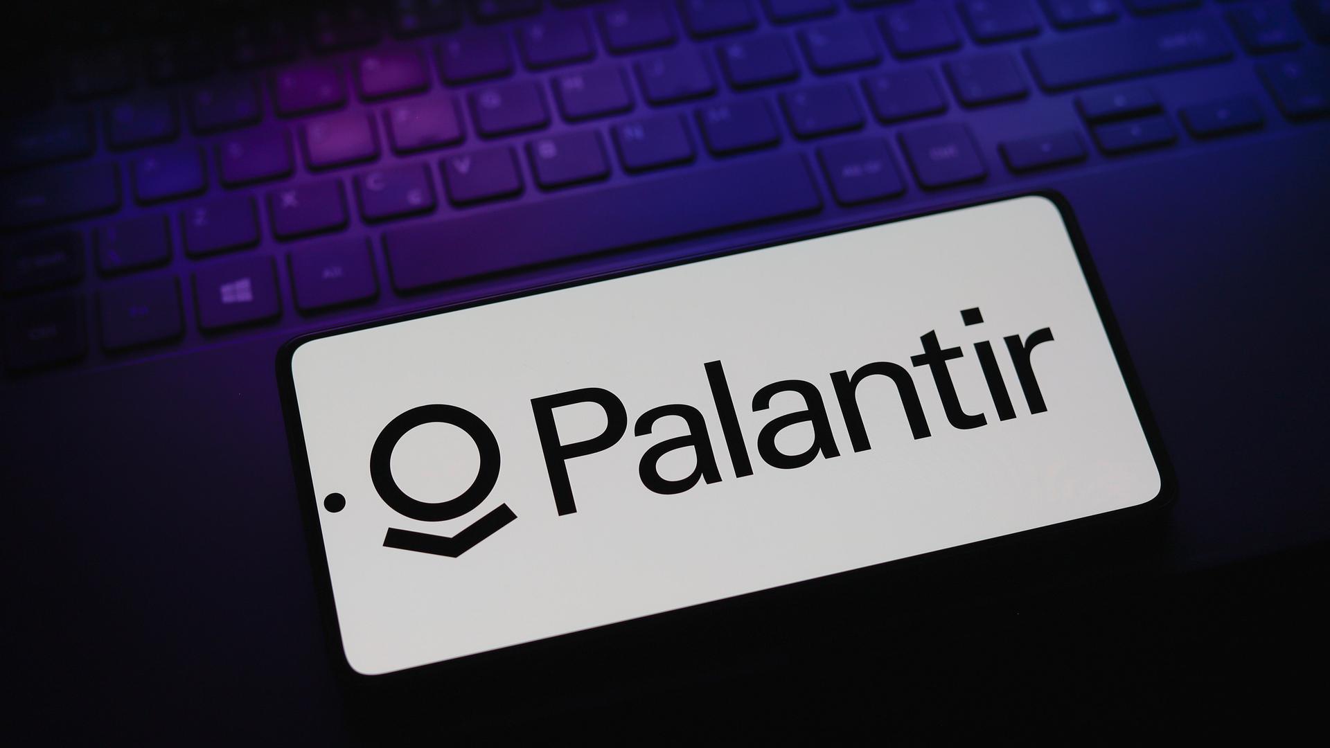 Das Logo der Firma Palantir Technologies erscheint auf einem Smartphone, das auf einer Computertastatur liegt.