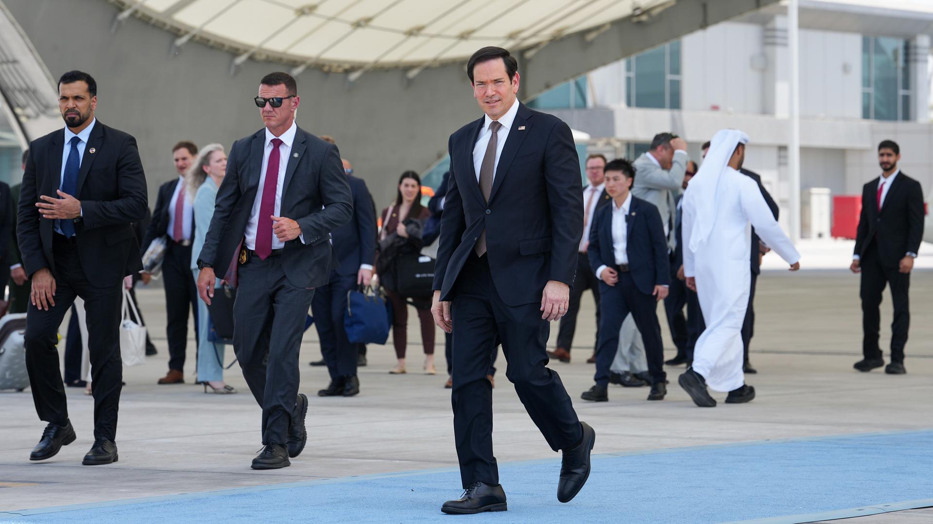 US-Außenminister Rubio geht auf dem Flughafen in Abu Dhabi zur Maschine, um nach Kuwait fliegen. Neben ihm laufen zwei Bodyguards. US-Außenminister Rubio geht auf dem Flughafen in Abu Dhabi zur Maschine, um nach Kuwait fliegen. Neben ihm laufen zwei Bodyguards.