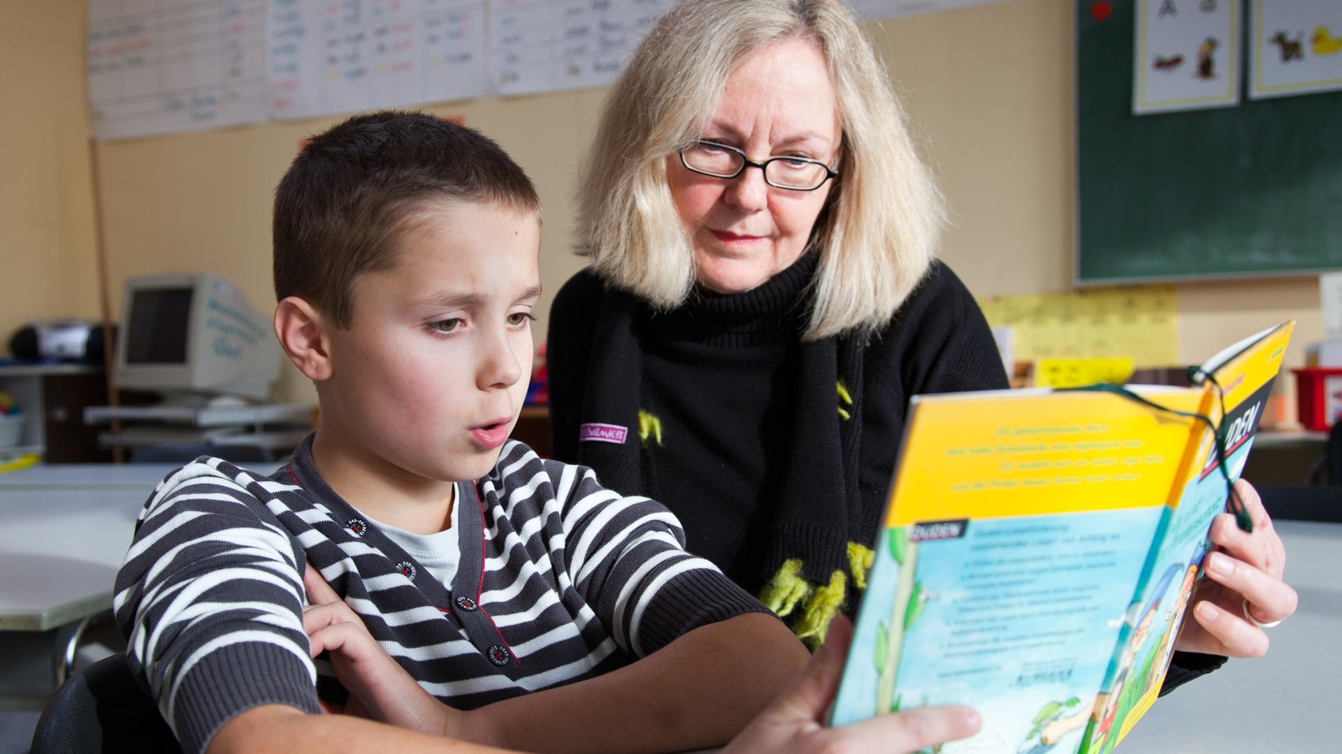 Ein Junge und seine Lesepatin lesen gemeinsam ein Buch an einer Grundschule in Münster.