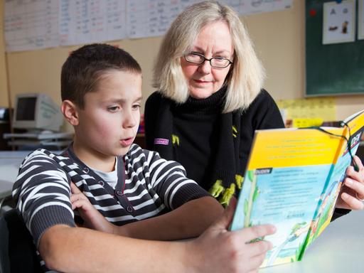 Ein Junge und seine Lesepatin lesen gemeinsam ein Buch an einer Grundschule in Münster.