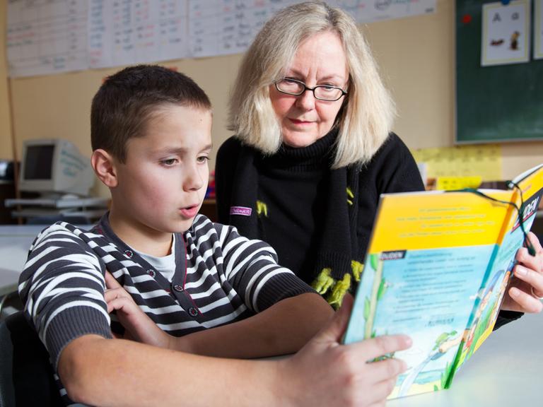 Ein Junge und seine Lesepatin lesen gemeinsam ein Buch an einer Grundschule in Münster.