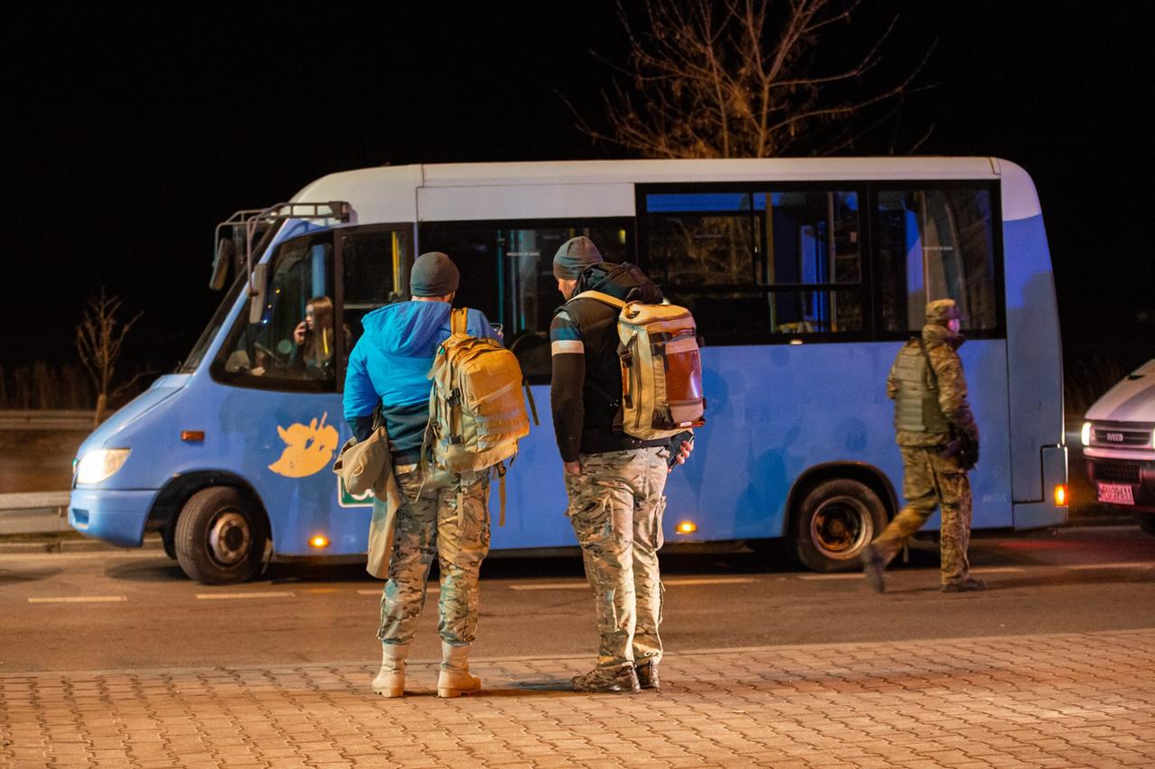 Zwei georgische Kämpfer auf dem Weg in die Ukraine. Die beiden stehen mit Rucksäcken vor einem Bus.