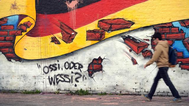 Ein Passant geht an einem Wandbild von Caspar Kirchner mit der deutschen Nationalflagge und dem Schriftzug "Ossi oder Wessi? vorbei. 