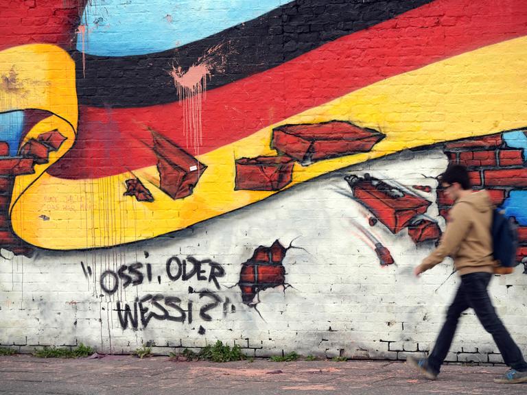 Ein Passant geht an einem Wandbild von Caspar Kirchner mit der deutschen Nationalflagge und dem Schriftzug "Ossi oder Wessi? vorbei. 