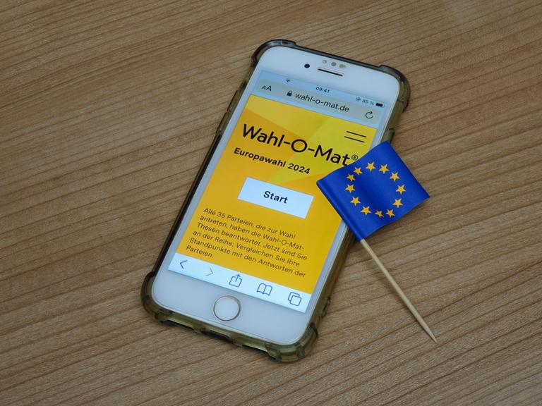 Auf einem Handy wird der Wahl-O Mat angezeigt, daneben befindet sich ein Fähnchen der Europaeischen Union.