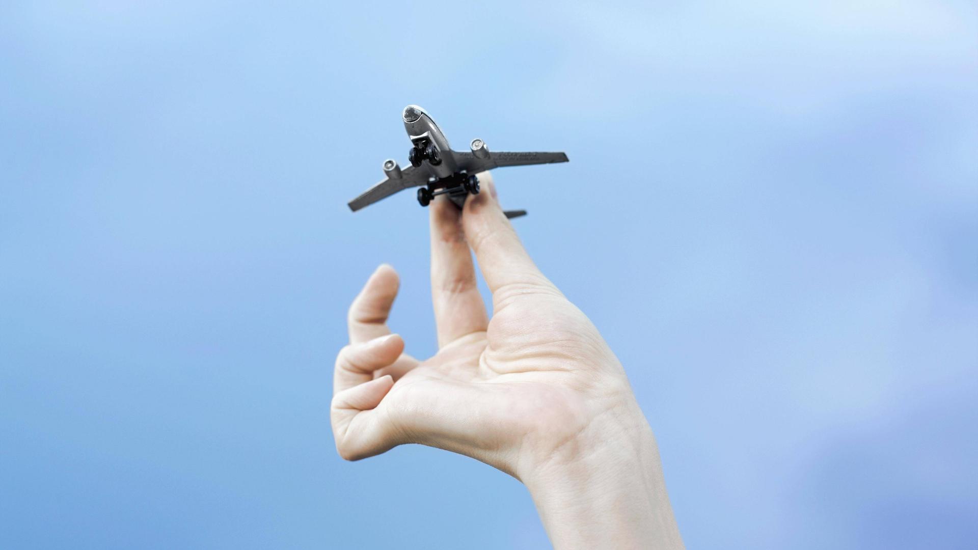 Eine Hand hält ein Modellflugzeug vor blauem Himmel.