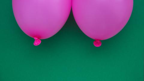 Zwei pinke Luftballons im Anschnitt, die zwei Brüste symbolisieren vor grünem Hintergrund.
