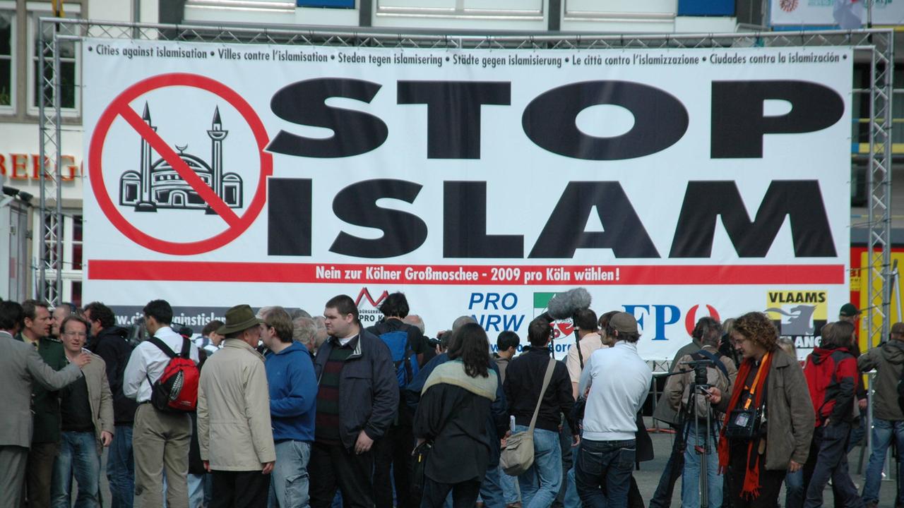 Ein Plakat zeigt die Aufschrift Stop Islam und ein rotes Verbotszeichen, das eine durchgestrichene Moschee zeigt. 