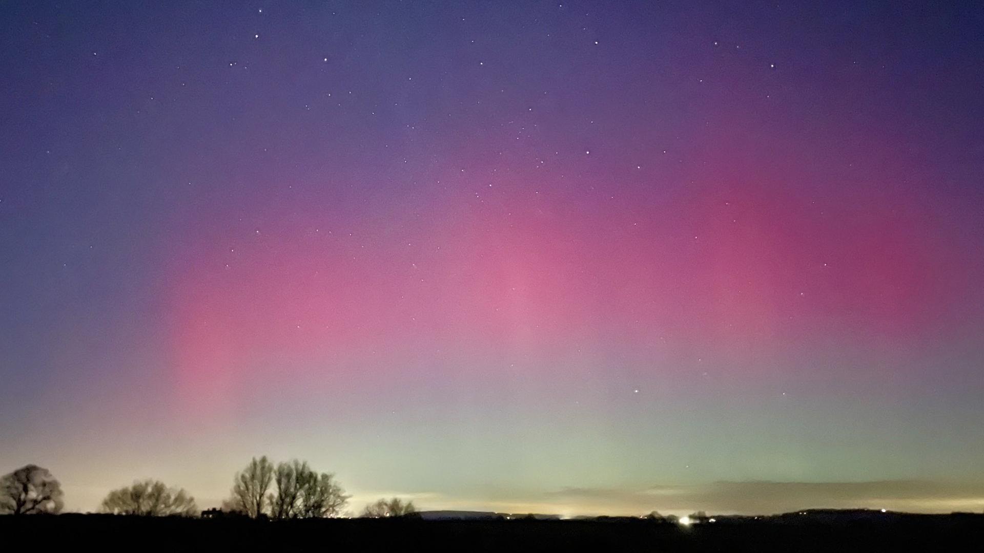 Über einer dunklen Landschaft leuchten Polarlichter.