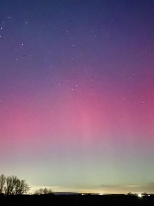 Über einer dunklen Landschaft leuchten Polarlichter.