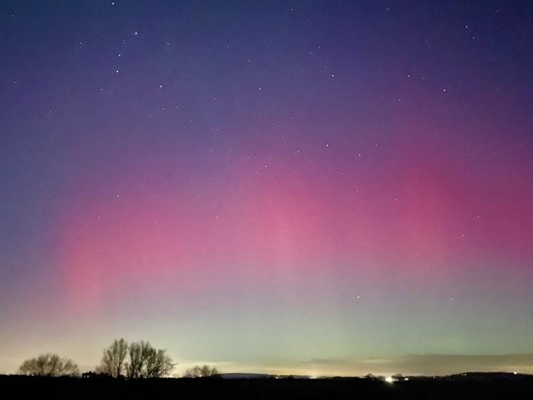 Über einer dunklen Landschaft leuchten Polarlichter.