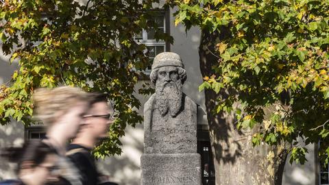Junge Menschen laufen zügig an dem Denkmal Gutenbergs vorbei, das auf dem großen Unigelände steht.