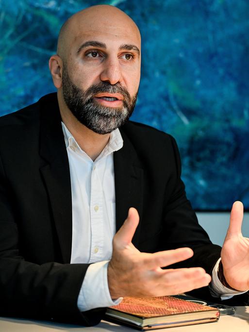 Der Psychologe und Extremismusforscher Ahmad Mansour sitzt an einem Tisch und spricht. 