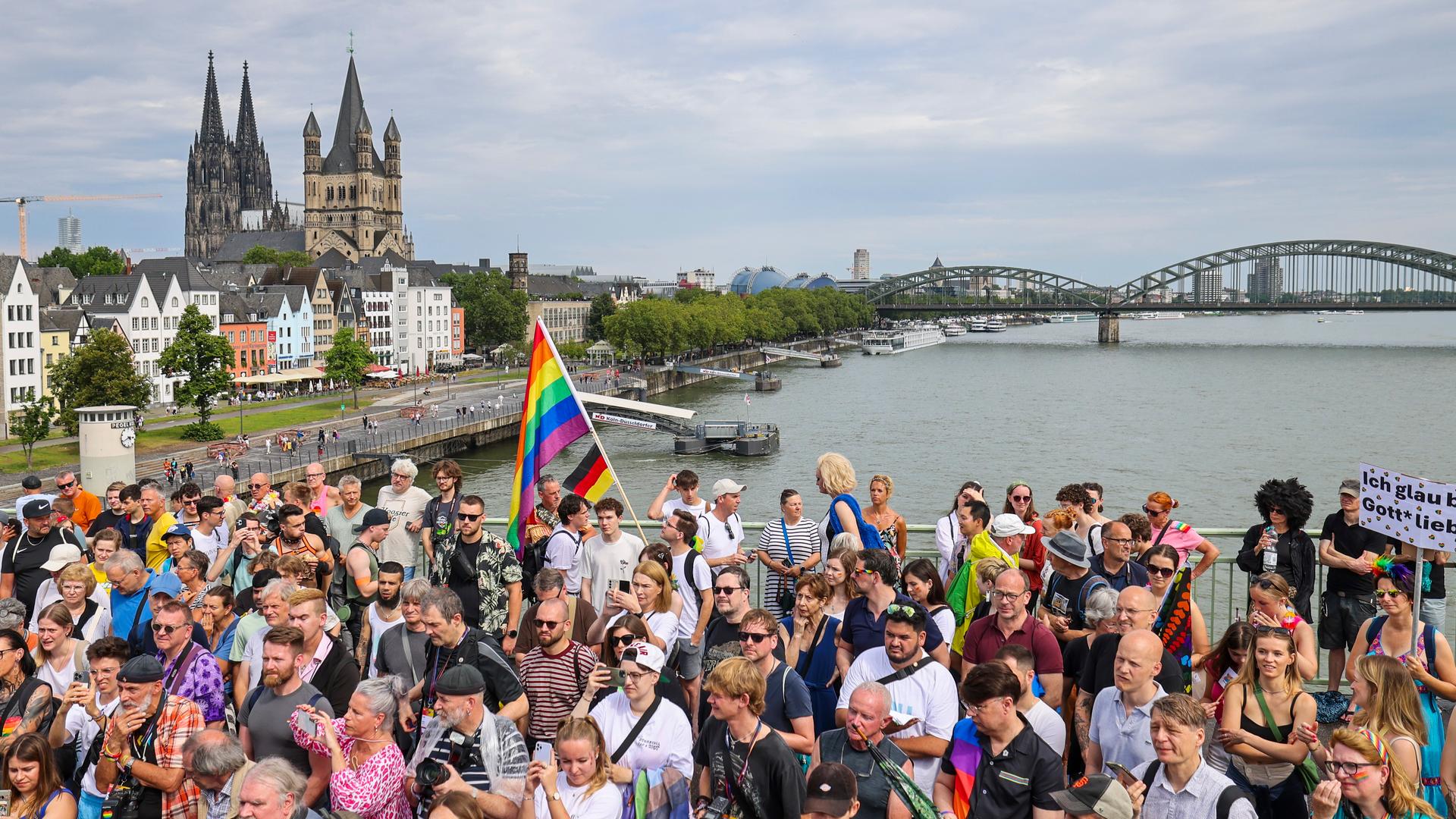 Eine Regenbogenflagge weht in einer Menschenmenge am Rhein. Im Hintergrund der Kölner Dom. Eine Regenbogenflagge weht in einer Menschenmenge am Rhein. Im Hintergrund der Kölner Dom.