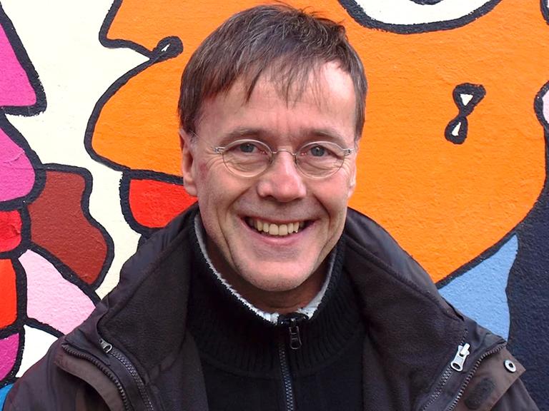 Porträt von Christoph Antweiler. Mittelalter weißer Mann vor einer Wand mit Graffiti Kunst.