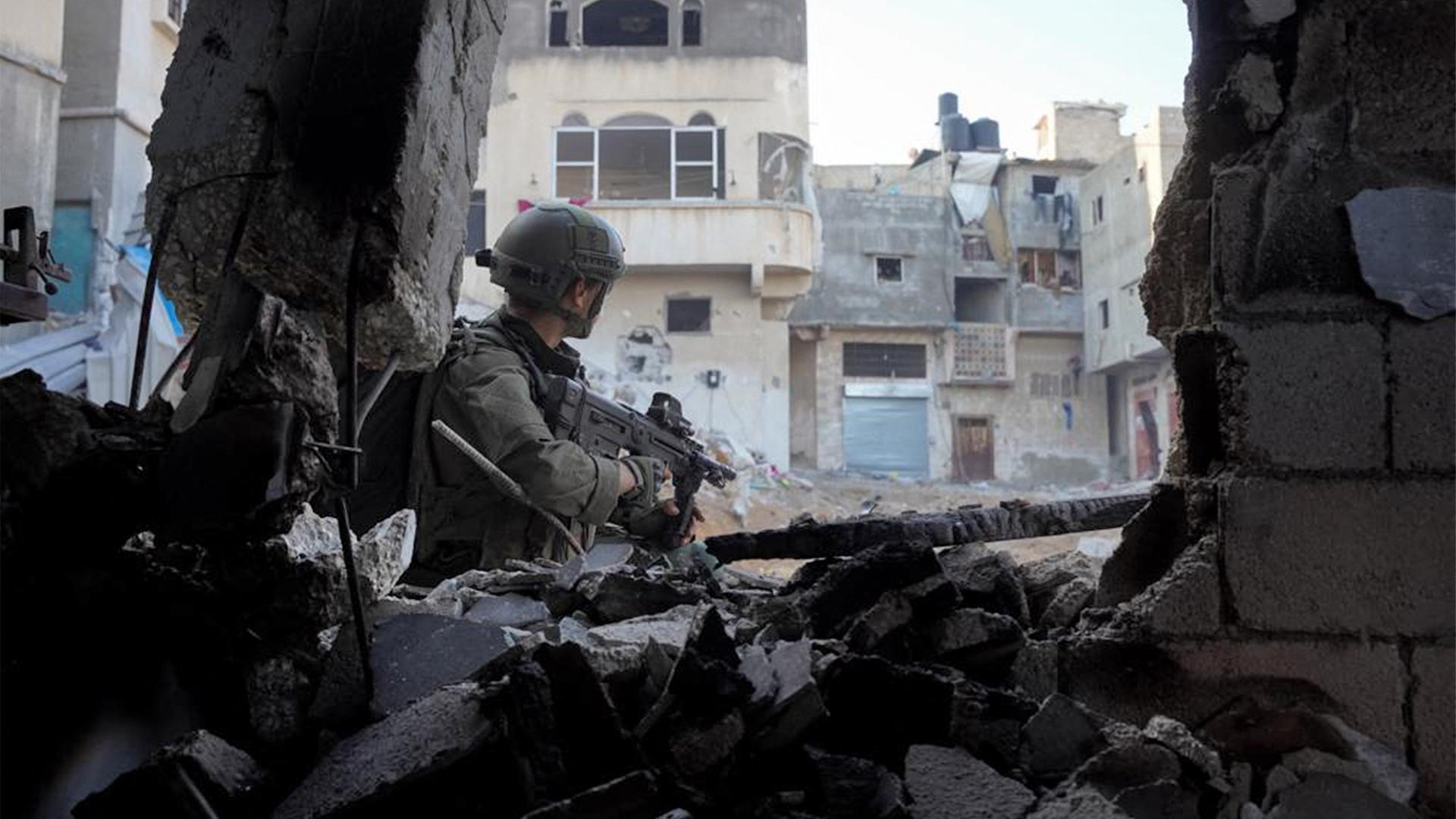 Ein israelischer Soldat steht mit der Waffe im Anschlag zwischen Trümmern und blickt auf Gebäude.