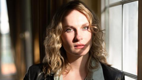 Porträt der Drehbuchautorin und Regisseurin Marie C. König. Sie steht neben einem Fenster, das Licht fällt auf ihre blonden Haare. Porträt der Drehbuchautorin und Regisseurin Marie C. König. Sie steht neben einem Fenster, das Licht fällt auf ihre blonden Haare.