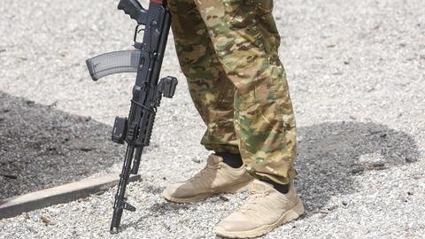 Das Bild zeigt nur die Beine des Soldaten in Tarnhosen. Er lehnt sein gewehr auf den Boden. 