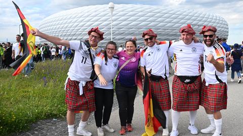 Eine Gruppe Fußballfans in Deutschland-Trikots und Schottenröcken steht vor der Münchner Fußball-Arena.
