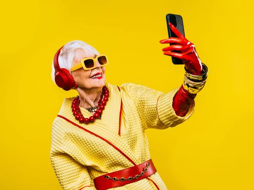 Ein fröhliche und lustige, ältere Dame mit modischer Kleidung und extravagante, jugendlichen Stil vor gelbem Hintergrund.