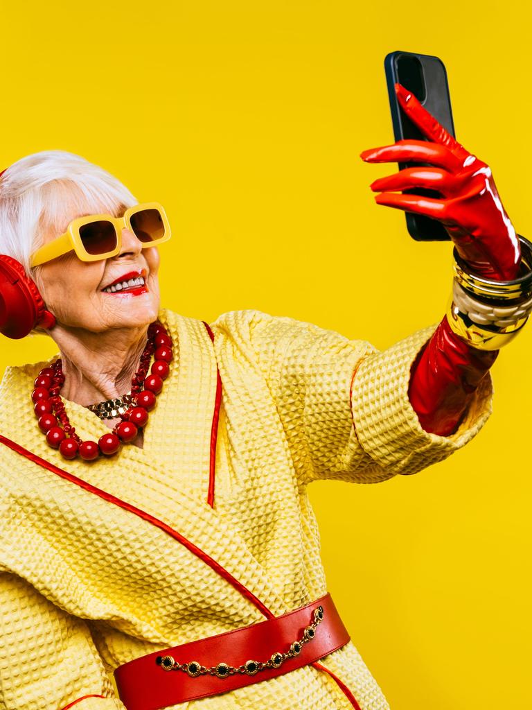 Ein fröhliche und lustige, ältere Dame mit modischer Kleidung und extravagante, jugendlichen Stil vor gelbem Hintergrund.