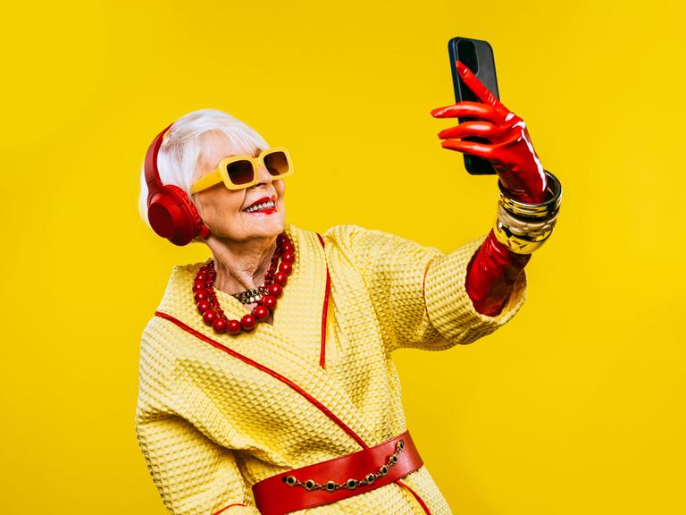Ein fröhliche und lustige, ältere Dame mit modischer Kleidung und extravagante, jugendlichen Stil vor gelbem Hintergrund.