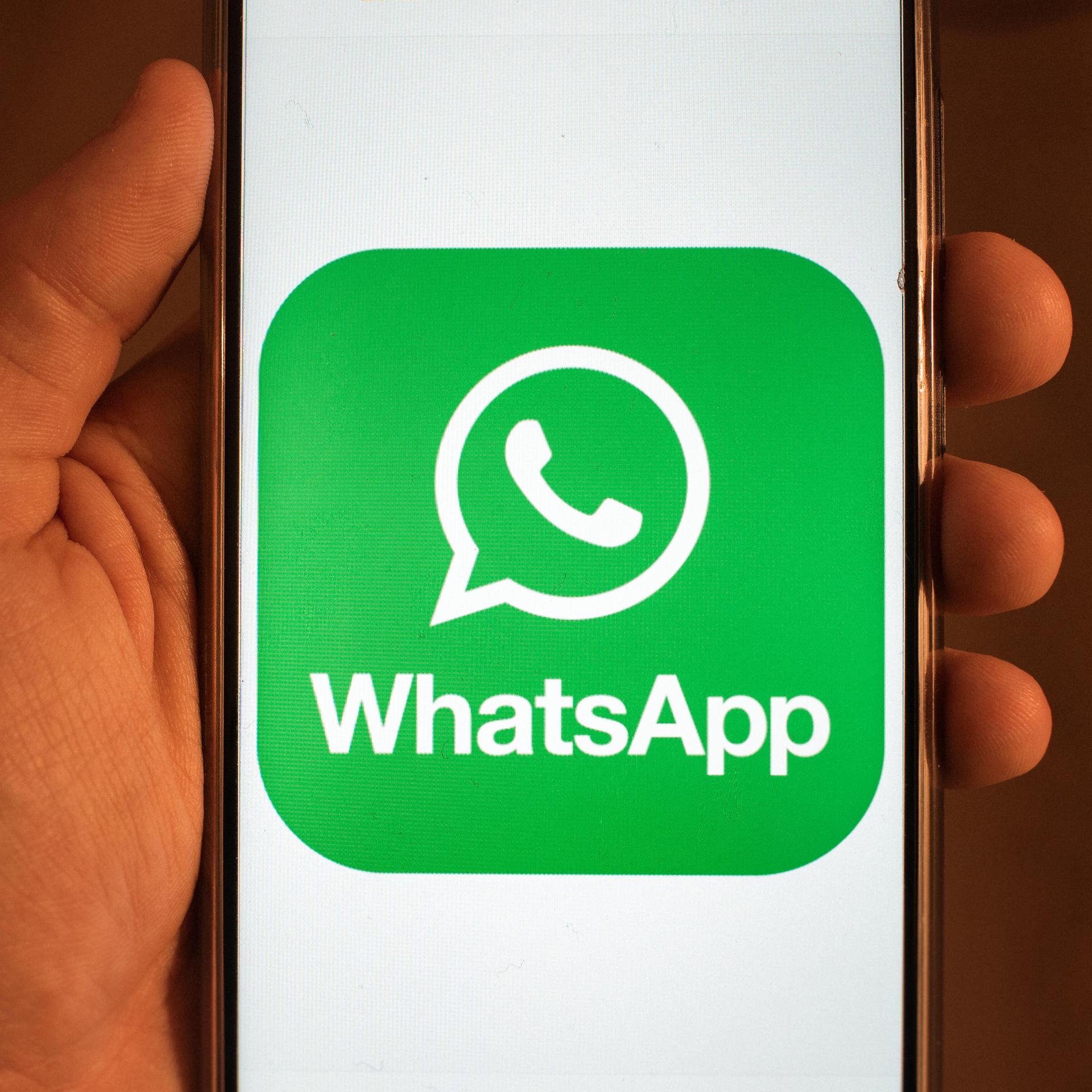 Eine Hand hält ein Handy. Darauf ist das Logo der App "WhatsApp" zu sehen.