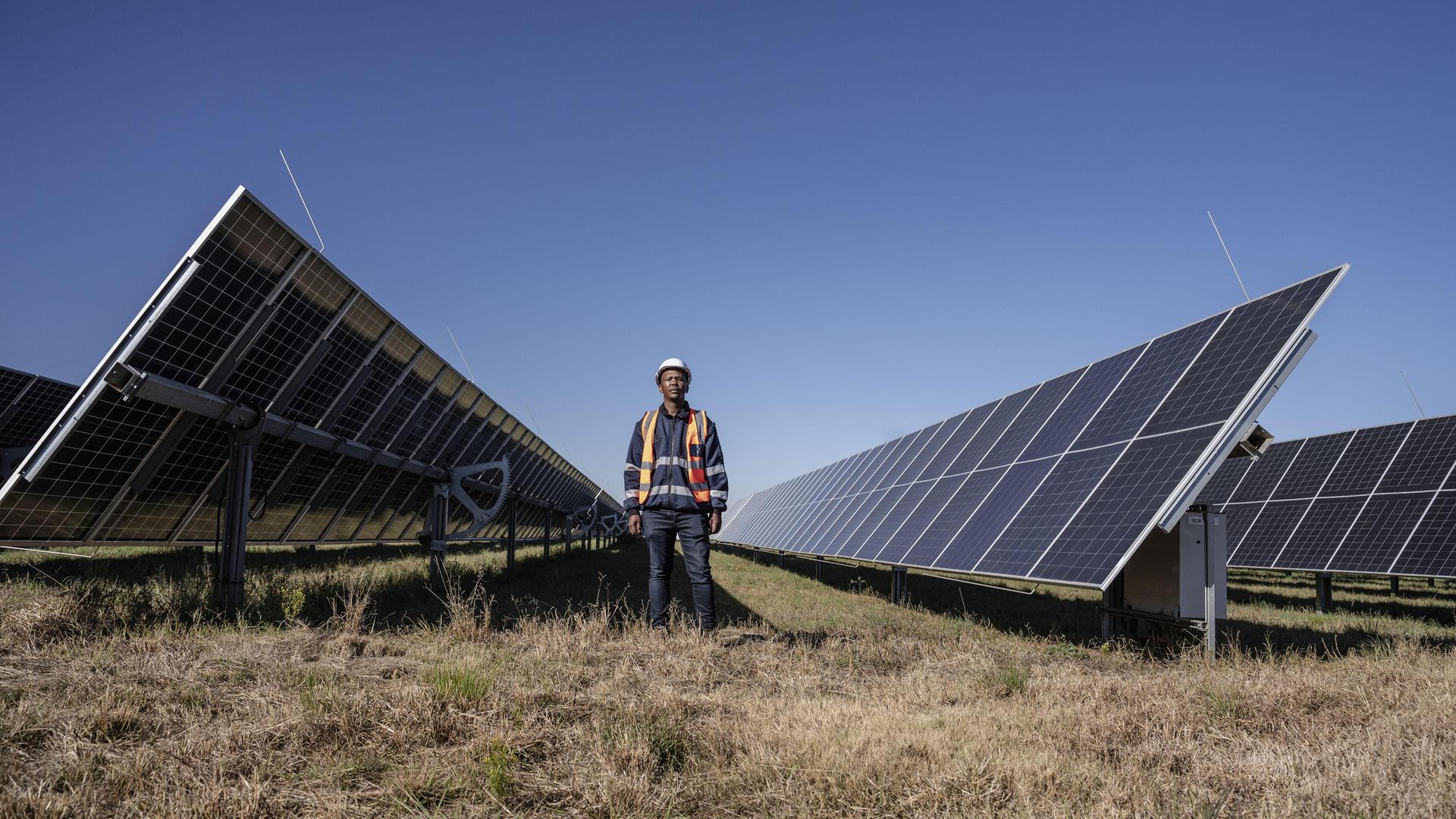 Ein Mann ist in der Nähe des Selemela-Solarkraftwerks zwischen riesigen Solarpanelen zu sehen. 