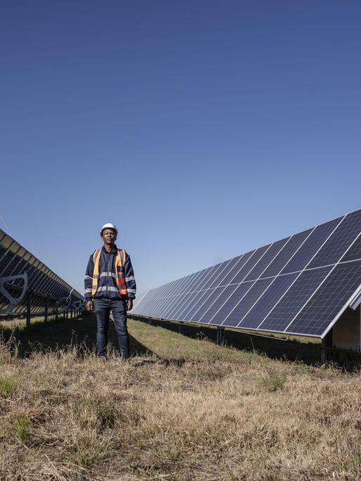 Ein Mann ist in der Nähe des Selemela-Solarkraftwerks zwischen riesigen Solarpanelen zu sehen. 
