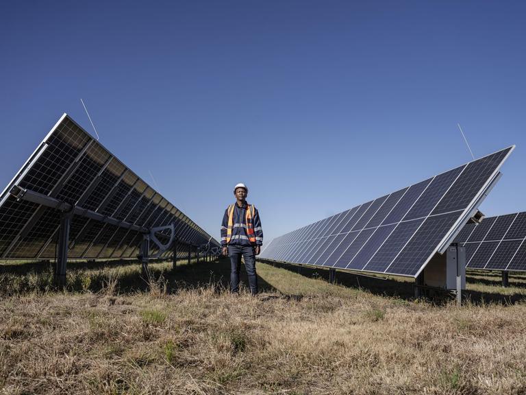 Ein Mann ist in der Nähe des Selemela-Solarkraftwerks zwischen riesigen Solarpanelen zu sehen. 